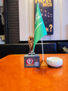 علم السعودية مع مجسم كأس وQR Code على طاولة داخل Mikel Coffee ضمن تجهيزات أجواء المباريات